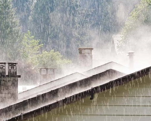 A house roof in woods under heavy rain, possibly symbolizing emergency plan for home during a natural disaster.