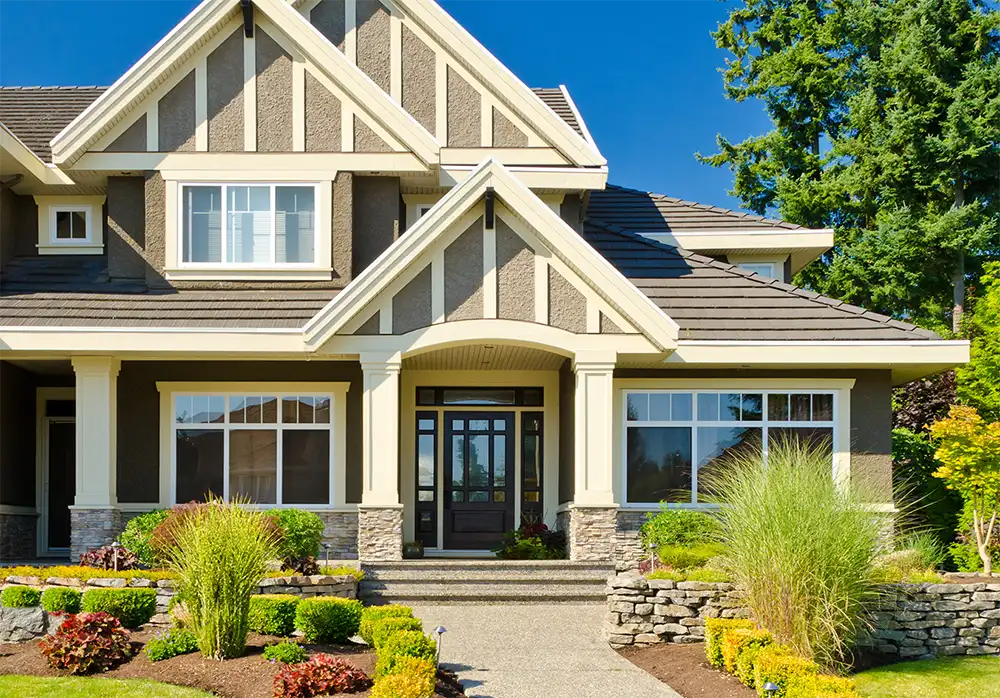 A modern home with beige and white detailing and lush landscaping