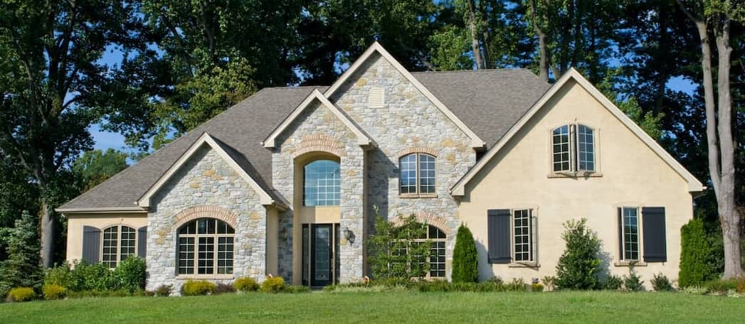 A newly built tan home surrounded by trees, showcasing a newly constructed property.