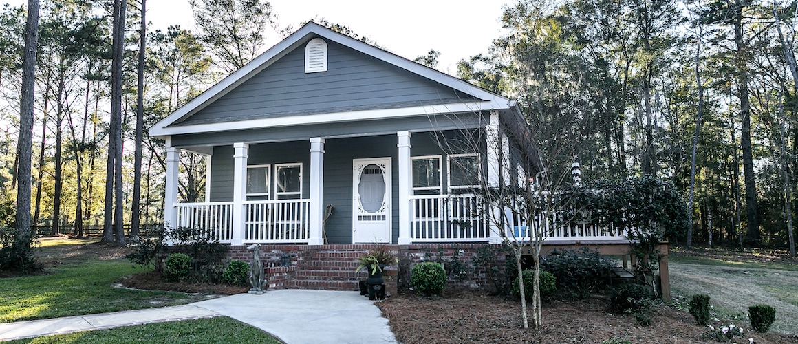 Small blue-gray mobile home with a front porch, potentially depicting a mobile or manufactured home design.