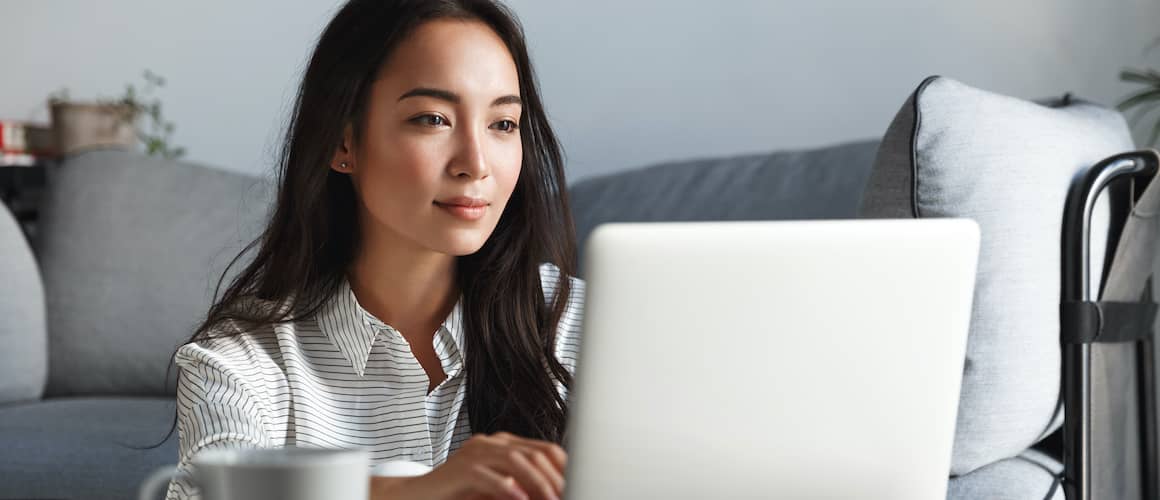 An asian woman looking at some information possibly related to real estate on her laptop.