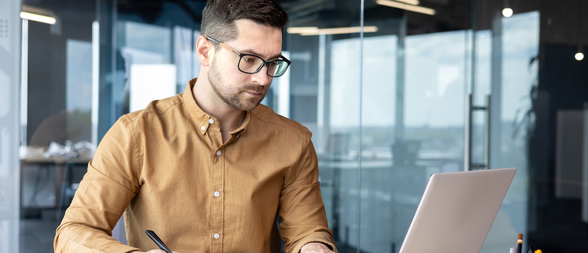 An analyst working in an office setting, focused on a laptop.