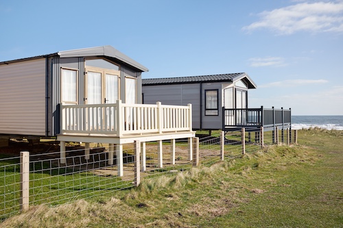 Two raised mobile homes with decks overlooking seaside.