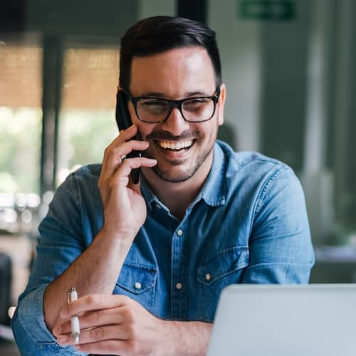 Young man smiling on the phone at a desk, possibly indicating work or communication.