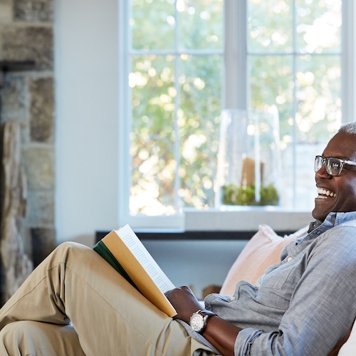 Senior man enjoying a book on his sofa in living room.