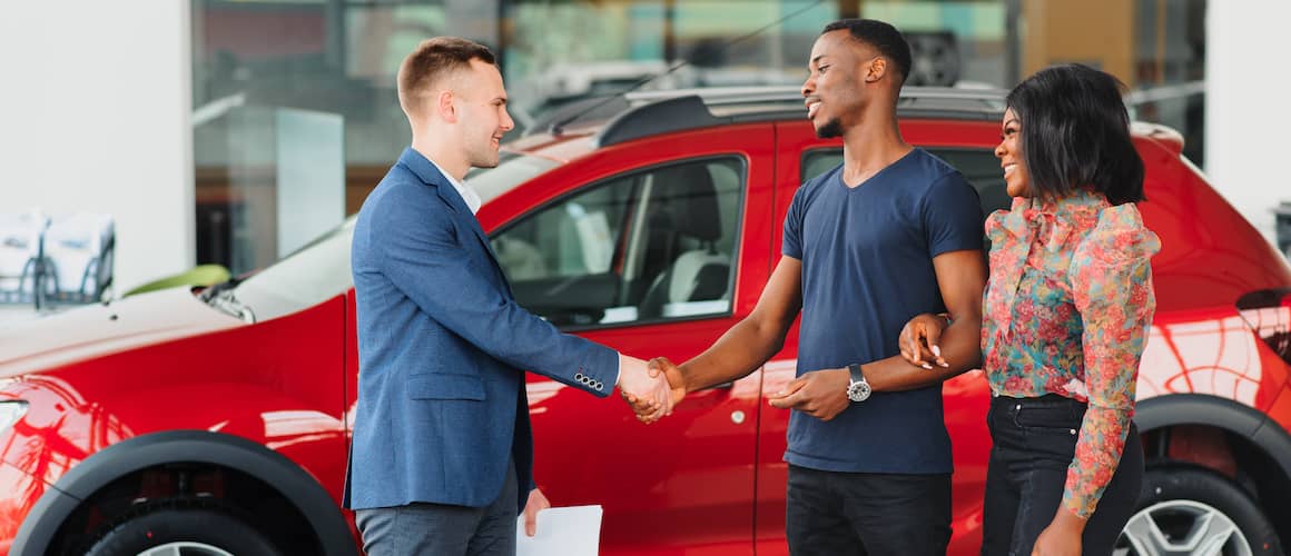 Young African-American couple buying new car at dealership.