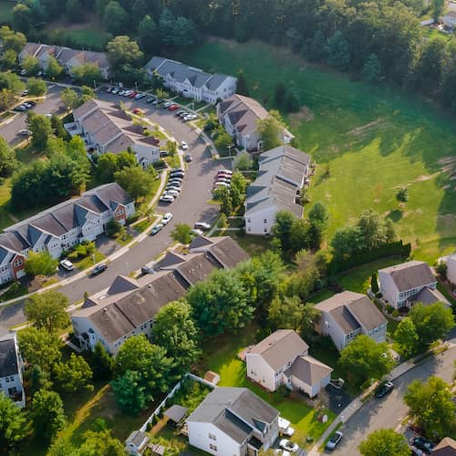 From above, a picturesque small town with neat streets, lined with colorful buildings and surrounded by greenery under a clear sky.