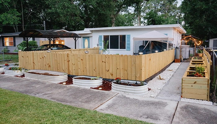 White ranch style home with blue shutters and raised garden beds out front.