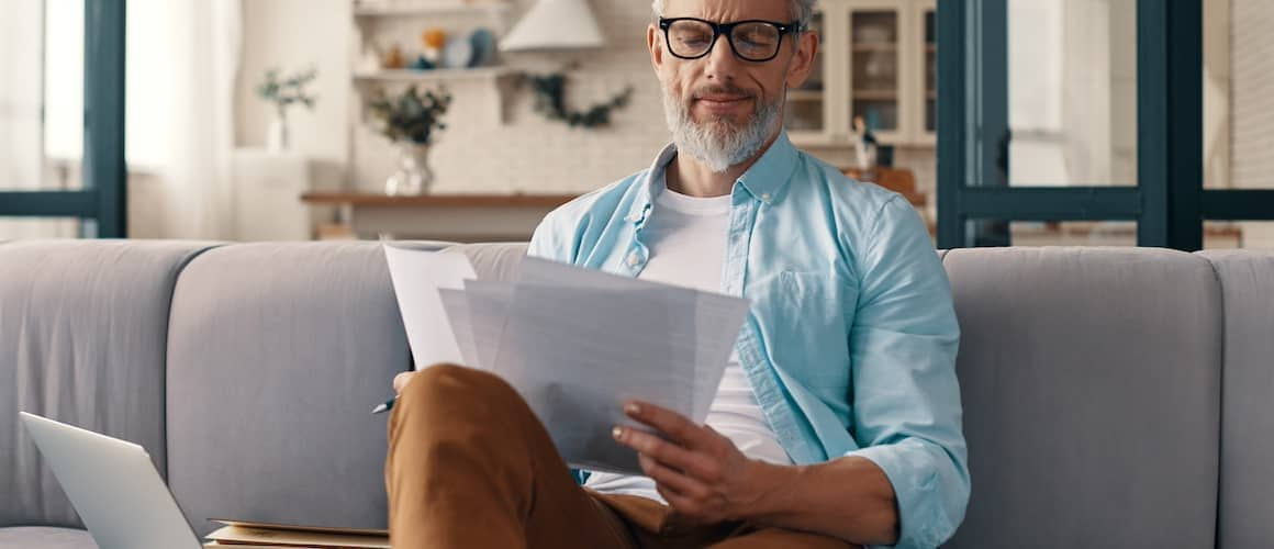 Middle-aged man applying for a loan while sitting on couch.