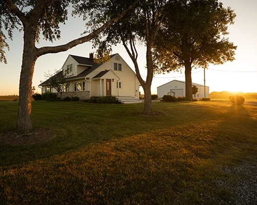 Beige house with golden sunlight falling over large lawn.