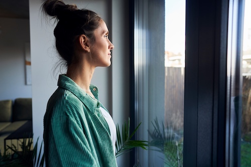 Young woman with top knot looking peacefully out window.