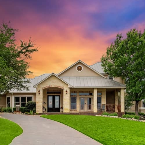 A beautiful brick home with tan stucco and a winding drive at sunset.