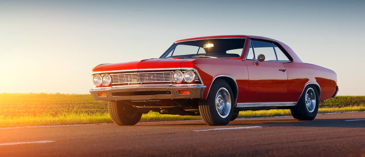 A red muscle car on the road in sunset lighting.