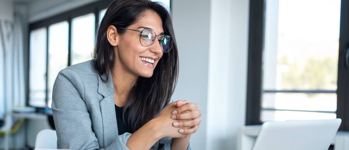 A woman smiling while looking at her laptop possibly chatting to someone.