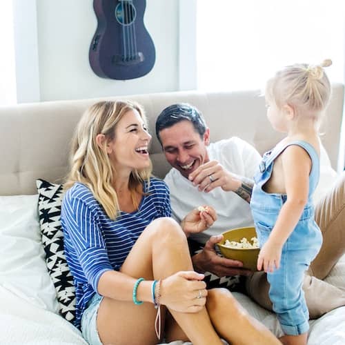 Young family enjoying a snack together on their couch, smiling.