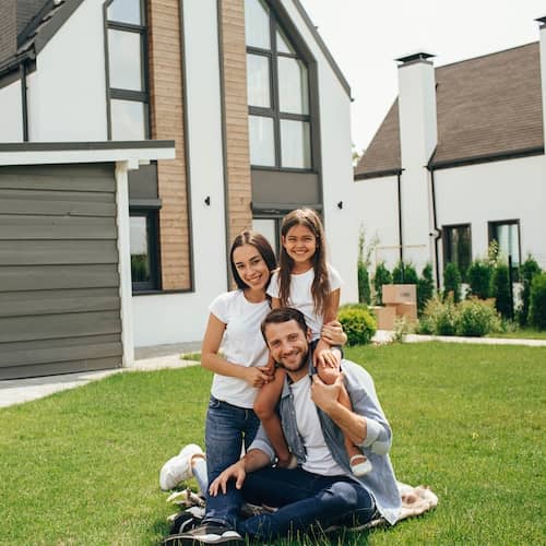 Young family in front of their new home and moving boxes by the front door.