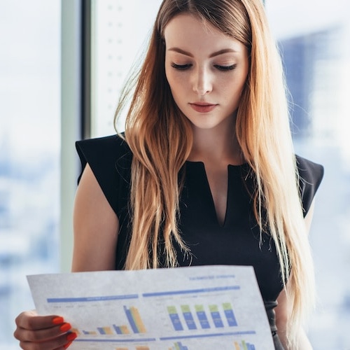 Woman looking over graphs for investments in office overlooking city skyline.
