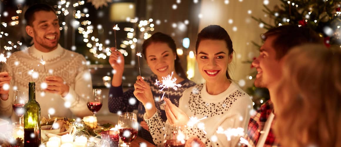 Friends at a holiday gathering holding sparklers around a table.