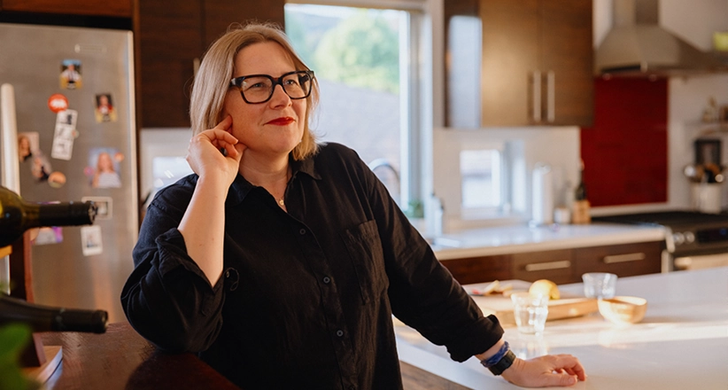 A woman standing in her kitchen looking off in the distance.