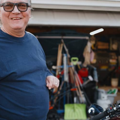 Man standing outside of garage with motorcycle.