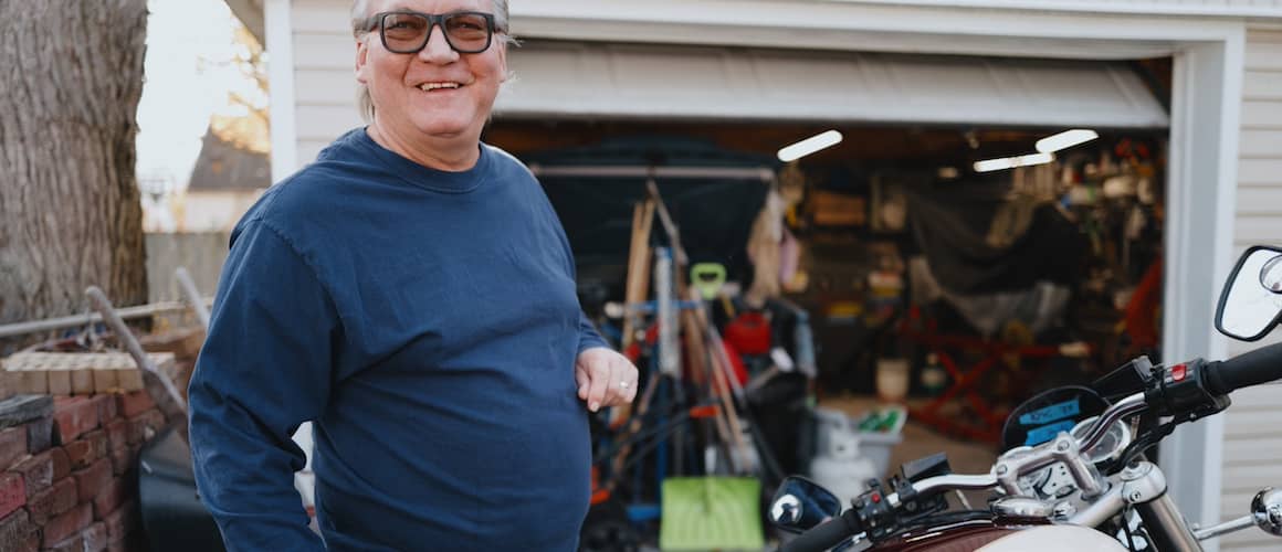 Man standing outside of garage with motorcycle.