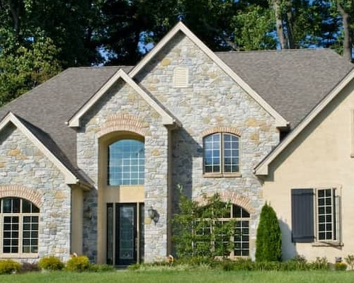 A newly built tan home surrounded by trees, showcasing a newly constructed property.