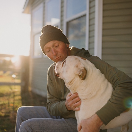 Man and large dog sitting on porch staring at each other.