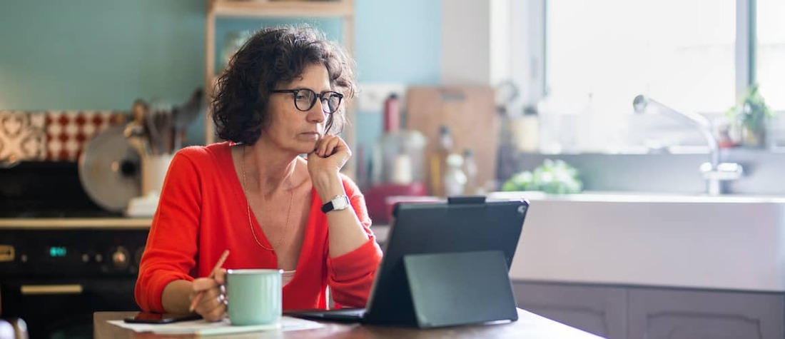 Middle aged woman sitting at computer holding a cup of coffee.