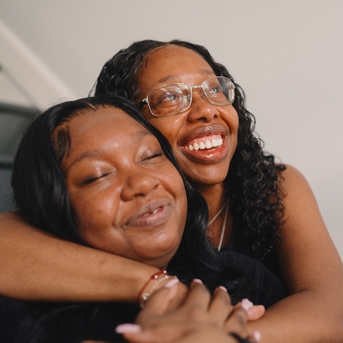 Woman with arm wrapped around another woman smiling.