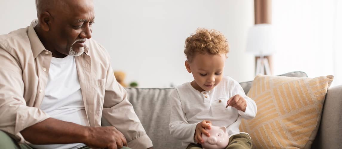 Grandfather watching as his grandchild puts coins into a ceramic piggy bank.