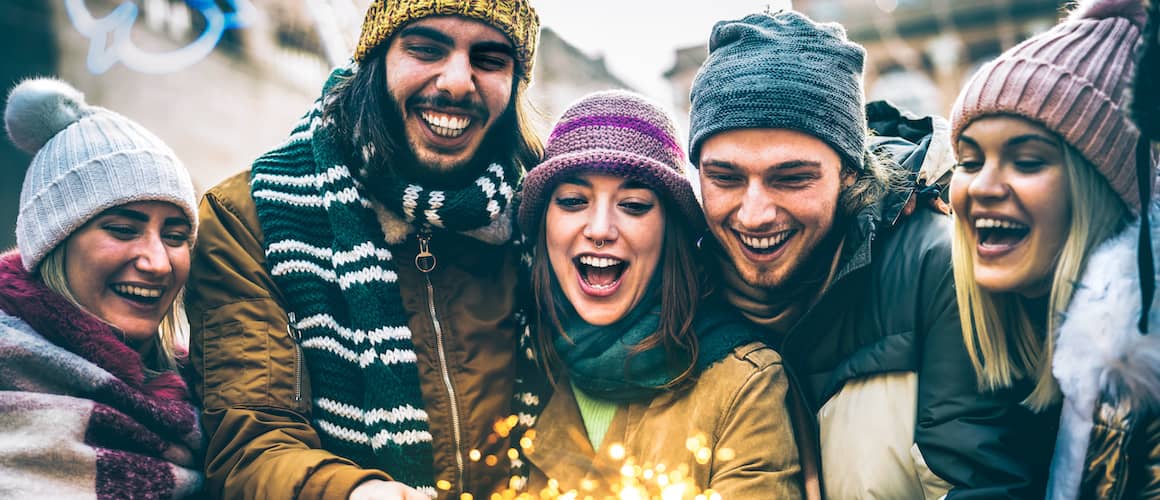 Group of friends in winter clothes lighting a sparkler for new years.