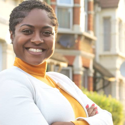 A woman standing in front of a row of houses, showcasing a peaceful neighborhood setting.