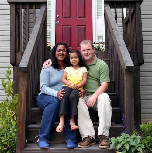 Young family of three sitting on front steps of a house.