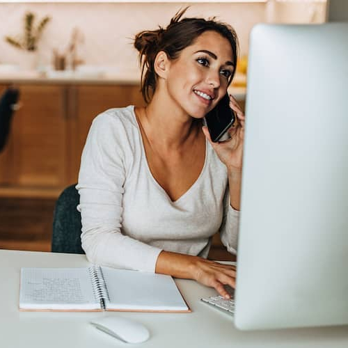 Woman using a phone and a MacBook, potentially managing finances or conducting research online.