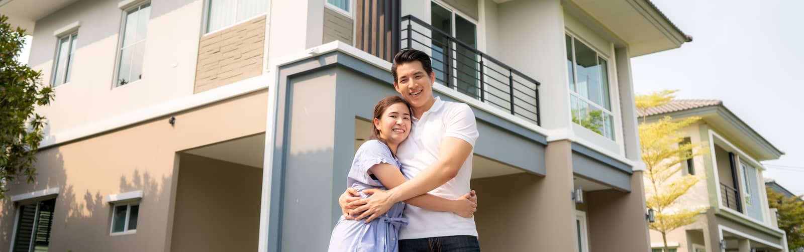 Young couple hugging in front of new modern home.