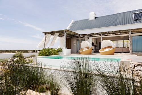 Modern beach house featuring pool and cabana chairs.