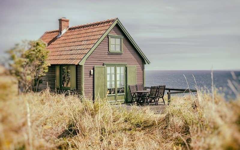 Quaint brown cottage with green shutters and deck overlooking the sea.