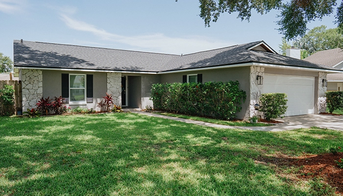 Ranch house with black shutters and green front lawn.