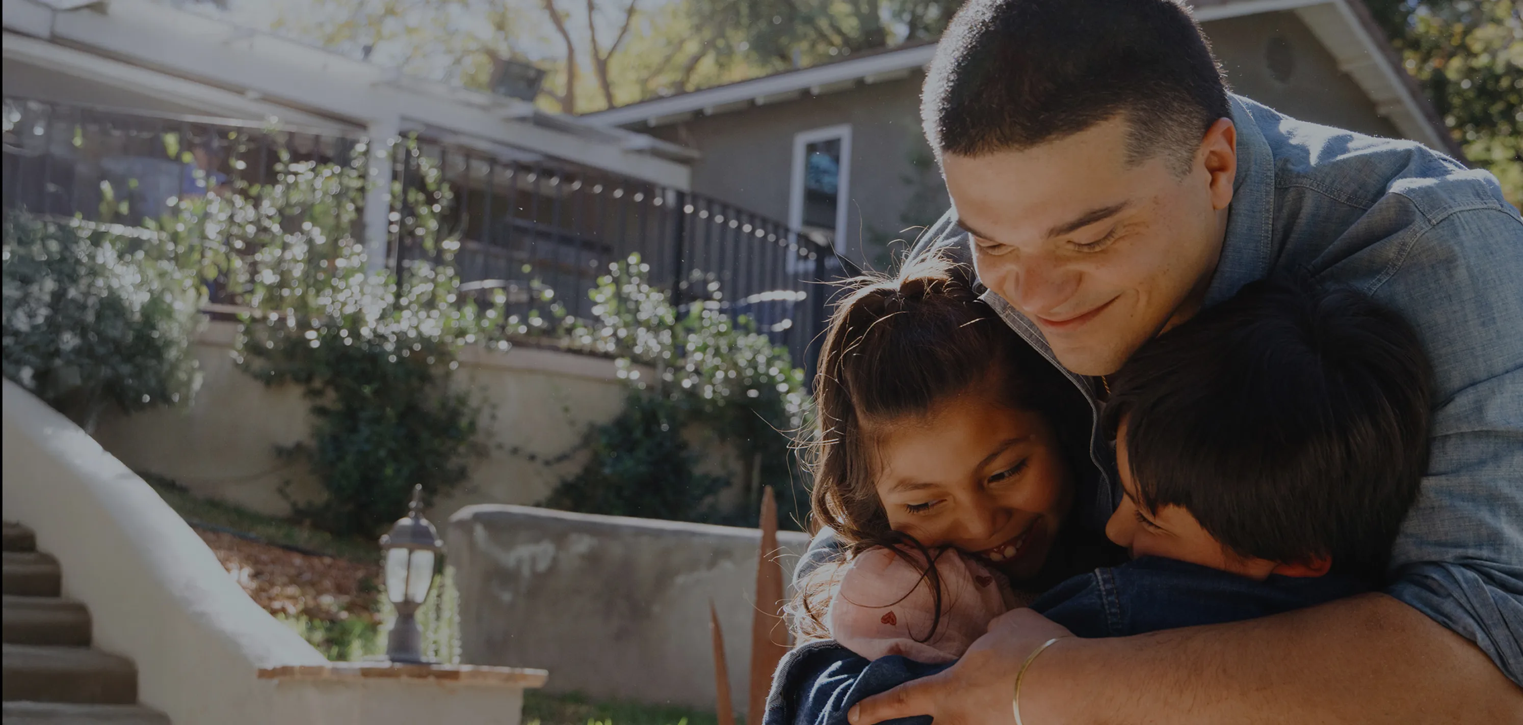 Man hugging his children tightly in front of a beautiful house.