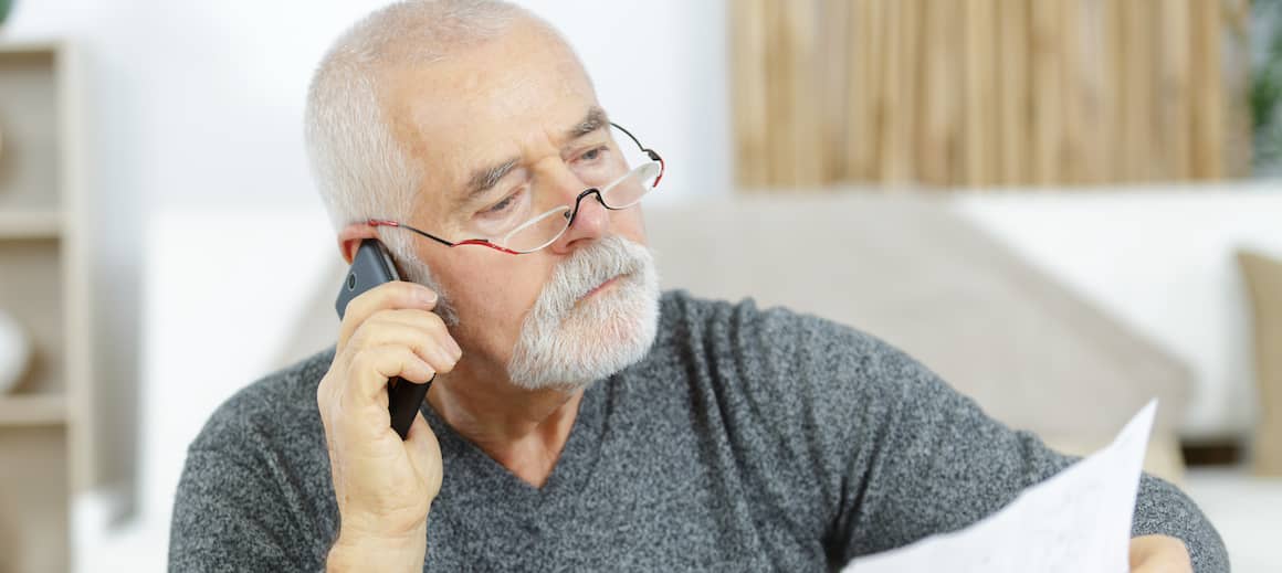 An older man on the phone looking at bills, potentially managing household expenses or discussing financial aspects of homeownership.