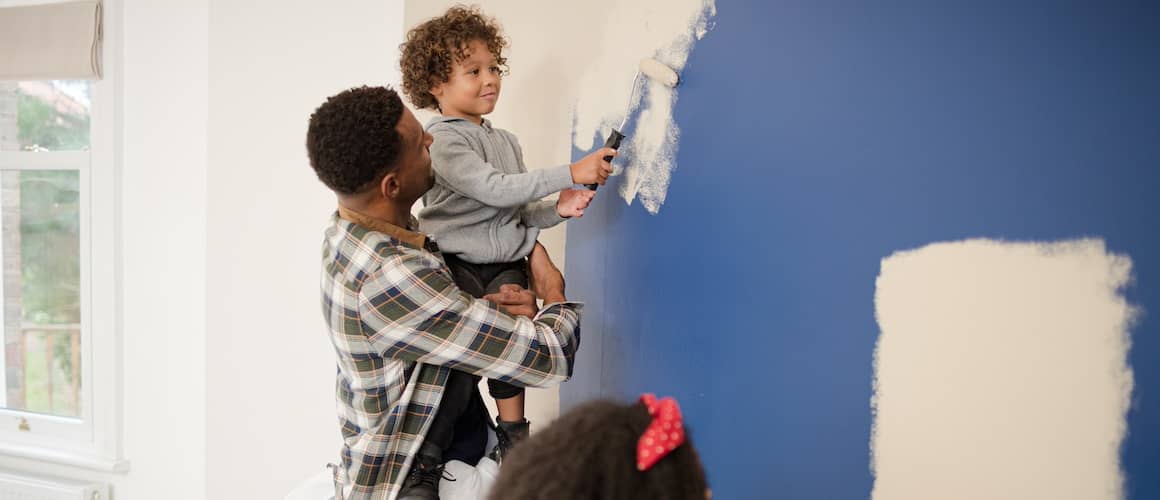 Father, son and daughter using rollers to paint blue walls in home white.