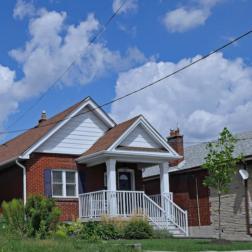 A line of houses set against a backdrop of clear blue sky and fluffy white clouds.