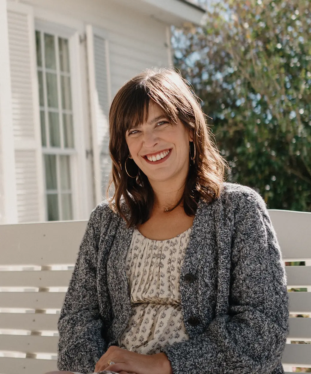 A woman sitting on the porch of her house, gently swinging on a wooden bench swing