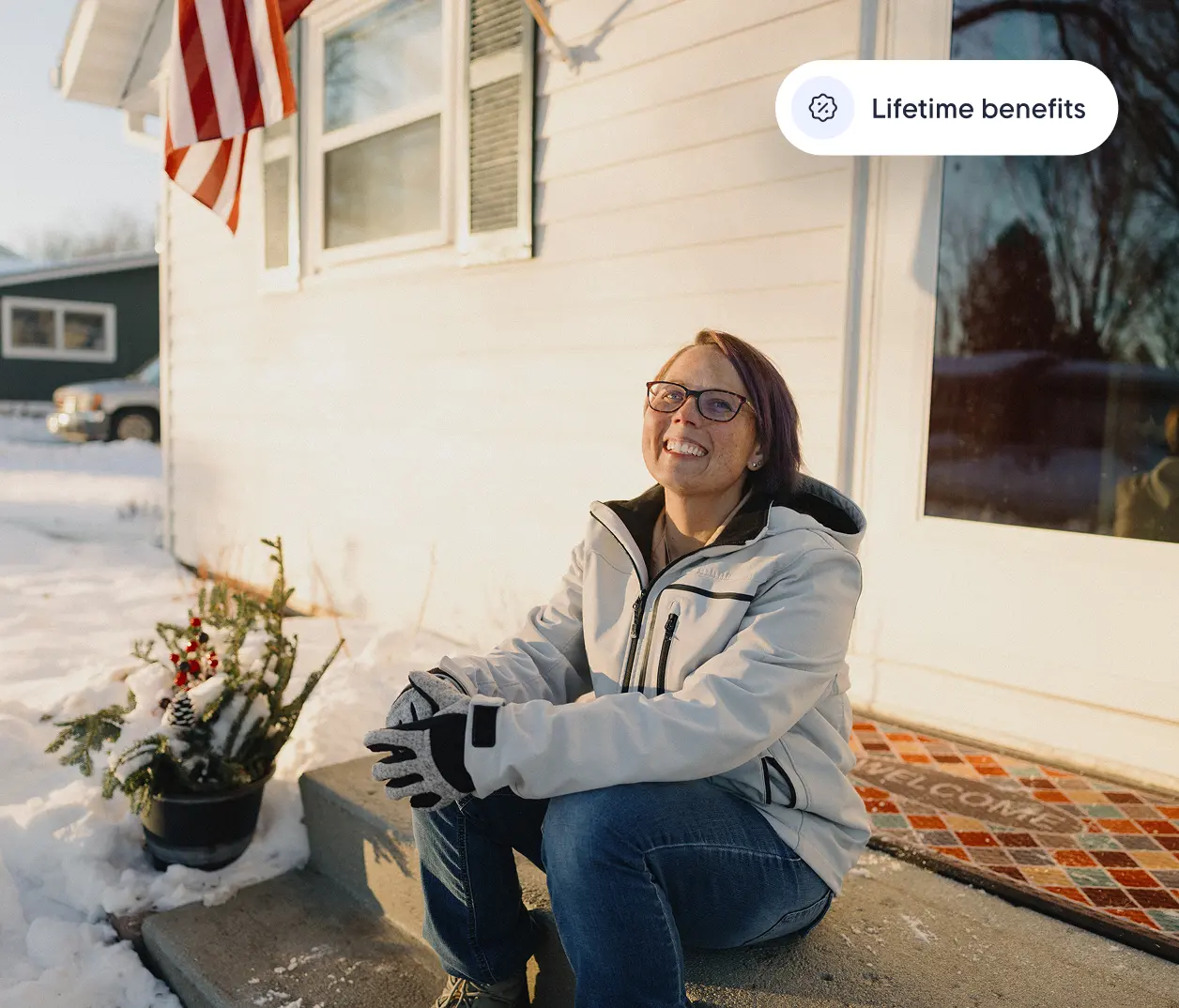 Smiling woman in winter jacket sitting on snowy front steps under an American flag, with text reading "Lifetime benefits."