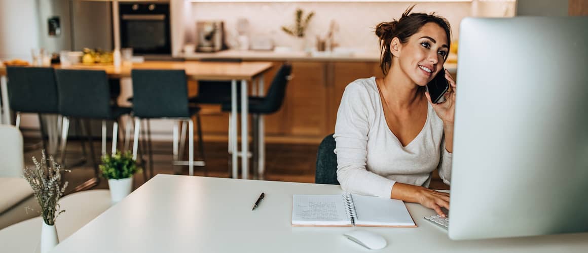 Woman using a phone and a MacBook, potentially managing finances or conducting research online.