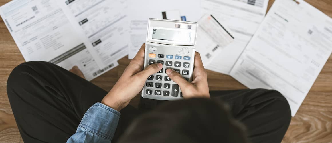 Man sitting on floor covered in papers holding calculator.