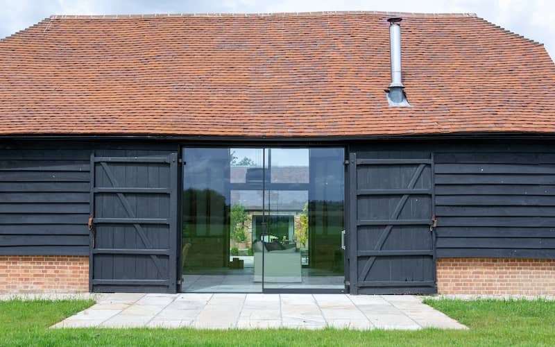 Barndominium with gray siding and large sliding glass doors through the middle of it. 