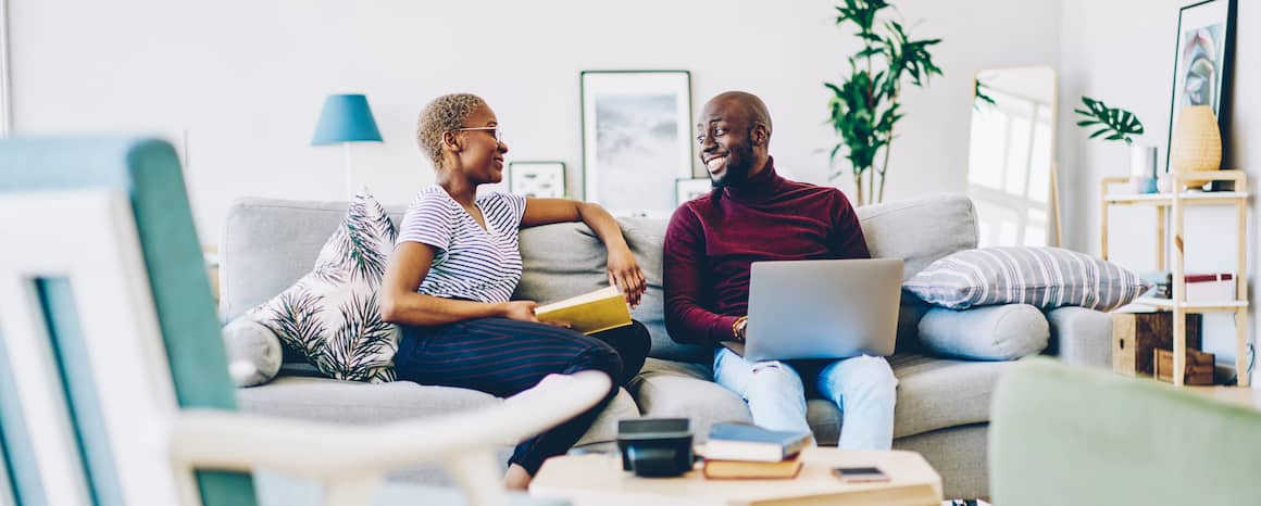 African American couple hanging out on the couch together with a laptop and a book.