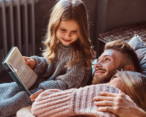A couple enjoying with their daughter who is holding a book.