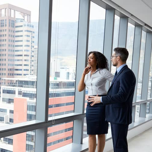 Possibly two real estate agents talking about something with a view of commercial real estate buildings from the window.